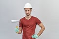 Young attractive man in red shirt, white protective helmet and gloves holding roller to paint with happy and confident expression. Royalty Free Stock Photo