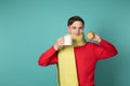 Young attractive man in red sweater and yellow scarf making funny face, holding white cup and sliced lemon in hands Royalty Free Stock Photo