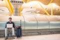 Young attractive man sitting at the airport working with a laptop waiting his flight with a suitcase Royalty Free Stock Photo