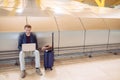 Young attractive man sitting at the airport working with a laptop waiting his flight with a suitcase Royalty Free Stock Photo