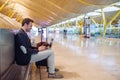 Young attractive man sitting at the airport working with a laptop waiting his flight with a suitcase Royalty Free Stock Photo