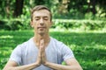 Attractive man in sport clothes is meditating cupped in a meditation or prayer gesture with a pacified face in the park