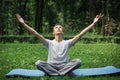 Young attractive man in sport clothes is meditating in the lotus position with a pacified face in the park against the background