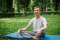 Young attractive man in sport clothes is meditating in the lotus position with a pacified face in the park
