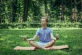 Young attractive man in sport clothes is meditating in the lotus position with a pacified face in the park