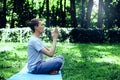 Young attractive man in sport clothes is meditating in the lotus position with a pacified face in the park