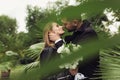 Young attractive man in trench coat dreamily kissing pretty woman in leather jacket holding bridal bouquet of white Royalty Free Stock Photo