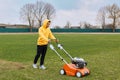 Young attractive man trimming grass with cutter, young adult male wearing yellow hoodie and black trousers mowning lawn, pushing Royalty Free Stock Photo