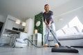 Young attractive man using a vacuum cleaner at home. Man cleaning house. House keeping concept Royalty Free Stock Photo