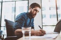 Young attractive man working at sunny loft office on laptop while sitting at wooden table.Businessman analyze digital