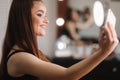 Young attractive model make a selfie after makeup in beauty studio. She use a ring lapm for photo. Background of white