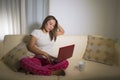 Young attractive and natural woman in pajamas pants relaxed on couch networking using laptop computer shopping online or ruling Royalty Free Stock Photo