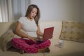 Young attractive and natural woman in pajamas pants relaxed on couch networking using laptop computer shopping online or working Royalty Free Stock Photo