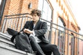 Young attractive pensive man sitting on steps and rummaging in his backpack. Royalty Free Stock Photo