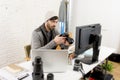 Young attractive press photographer holding photographic camera viewing his work on editor office desk