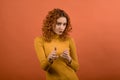 Young and attractive redhead Caucasian girl in orange jumper showing hands with fingers pistols isolated on orange studio backgrou