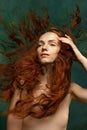 Young attractive redhead girl with long curly hair wearing nude color lingerie  over dark green background Royalty Free Stock Photo