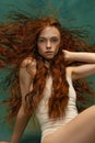 Young attractive redhead girl with long curly hair wearing nude color lingerie  over dark green background Royalty Free Stock Photo