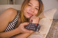 Young attractive and relaxed Asian Indonesian woman holding TV remote watching television movie or series episode enjoying and Royalty Free Stock Photo