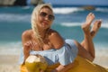 Young attractive and relaxed blond woman in bikini lying on beanbag hammock at tropical paradise beach drinking coconut water Royalty Free Stock Photo