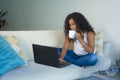 Young attractive and relaxed latin American student woman sitting at home sofa couch networking with laptop computer drinking coff