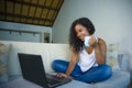 Young attractive and relaxed latin American student woman sitting at home sofa couch networking with laptop computer drinking coff