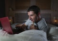 Young attractive and relaxed man networking at home lying comfortable on bed late night happy watching movie on laptop computer or Royalty Free Stock Photo