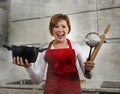 Young attractive rookie home cook woman in red apron at home kitchen holding cooking pan and rolling pin screaming desperate Royalty Free Stock Photo