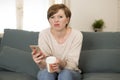 Young attractive 30s red hair woman upset bored and moody using internet app on mobile phone sitting at home sofa couch in annoyed Royalty Free Stock Photo