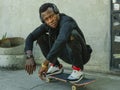 Young attractive and serious black African American man squatting on skate board at grunge street corner looking cool posing in Royalty Free Stock Photo