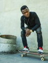 Young attractive and serious black African American man squatting on skate board at grunge street corner looking cool posing in Royalty Free Stock Photo