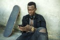 Young attractive and serious black afro American man sitting on grunge street ground corner with skate board in badass bad boy Royalty Free Stock Photo