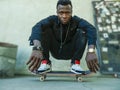 Young attractive and serious black afro American man squatting on skate board at grunge street corner looking cool posing in Royalty Free Stock Photo