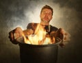 Young attractive and shocked messy home cook man with apron holding cooking pot in fire burning the food in kitchen disaster Royalty Free Stock Photo