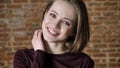 Young attractive shy girl is giggling, watching at camera, brick background