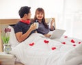 Attractive sitting on bedroom holding cups of coffee looking to each other with love , many red hearts on blanket,Valentine`s day