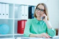 Young attractive smiling business woman in glasses sitting at office chair working at desktop computer talking on mobile Royalty Free Stock Photo