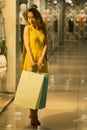 Young Attractive Smiling Girl in Yellow Dress is Walking in the Mall with Shopping Bags Royalty Free Stock Photo