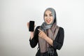 Young attractive smiling Muslim student wearing turban hijab headscarf showing and pointing at smartphone with her