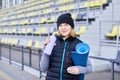 Young attractive smiling woman doing sports in morning sunrise on the park, holding yoga mat and bottle of water Royalty Free Stock Photo