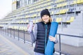 Young attractive smiling woman doing sports in morning sunrise on the park, holding yoga mat and bottle of water Royalty Free Stock Photo