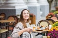 Young attractive smiling woman in gray knitted sweater drinking tea outdoors at the street cafe