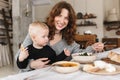 Young attractive smiling woman with red hair in knitted sweater sitting at the table feeding her little son happily Royalty Free Stock Photo