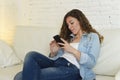 Young attractive spanish woman using mobile phone app or texting on home couch Royalty Free Stock Photo