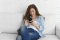 Young attractive spanish woman using mobile phone app or texting on home couch Royalty Free Stock Photo