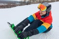 Young attractive sportsman sitting on the snow and putting on snowboard on feet Royalty Free Stock Photo