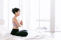 Young attractive sporty Asian woman practicing yoga on the bed, doing Ardha Padmasana exercise, meditating in Half Lotus pose. Royalty Free Stock Photo