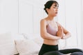 Young attractive sporty Asian woman practicing yoga on the bed, doing Ardha Padmasana exercise, meditating in Half Lotus pose. Royalty Free Stock Photo