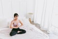 Young attractive sporty Asian woman practicing yoga on the bed, doing Ardha Padmasana exercise, meditating in Half Lotus pose. Royalty Free Stock Photo