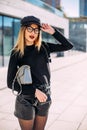 Young attractive stylish smiling woman having fun in city , positive, emotional, long hair, wearing leather shorts and black Royalty Free Stock Photo